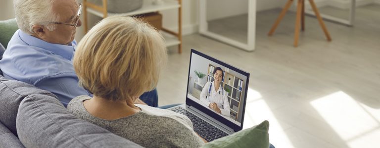 Senioren Paar sitzen auf der Couch und habe eine Online-Sprechstunde über den Laptop mit der Ärztin