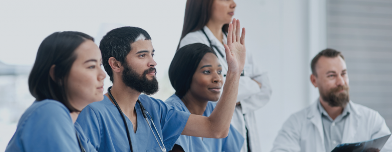 Auf dem Bild sehen Sie mehrere Personen die im Gesundheitswesen arbeiten und sich für E-Learning interessieren. Eine Person hält fragend die Hand nach oben.