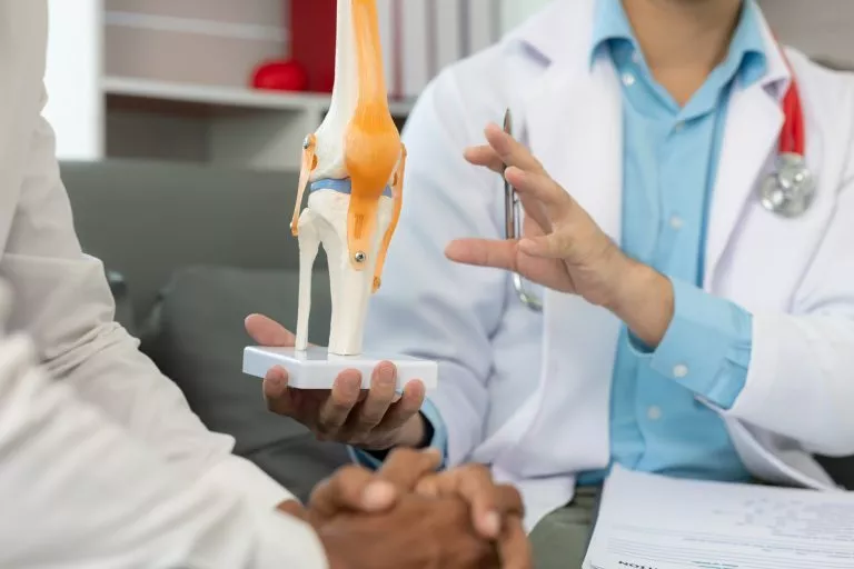 Male doctor and male patient discussing knee joint model It is likely that the focus will be on the condition of arthritis in the knee during a medical consultation at a hospital or clinic