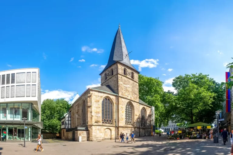 Historische Kirche mit Turm neben modernen Gebäuden in einer Innenstadt: Essener Dom.