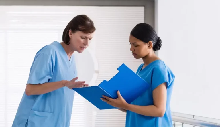 Zwei Pflegekräfte im Gespräch, eine zeigt auf eine Akte.