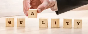 Hand setzt Holzbaustein mit Buchstabe A in das Wort "QUALITY".