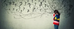 Person mit gesenktem Kopf, umgeben von Fragezeichen und chaotischen Zeichnungen.