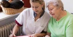 Pflegekraft erklärt älterer Frau ein Dokument, beide schauen gemeinsam darauf.
