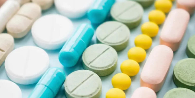 Verschiedenfarbige Tabletten und Kapseln liegen sortiert auf einer hellblauen Fläche.