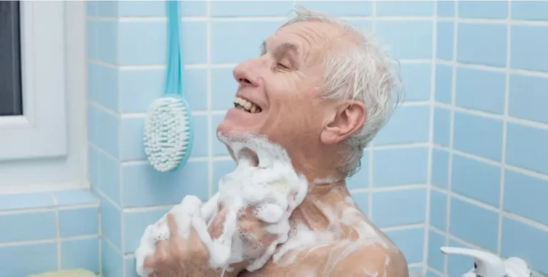 Ältere Person wäscht sich lachend unter der Dusche mit viel Schaum.