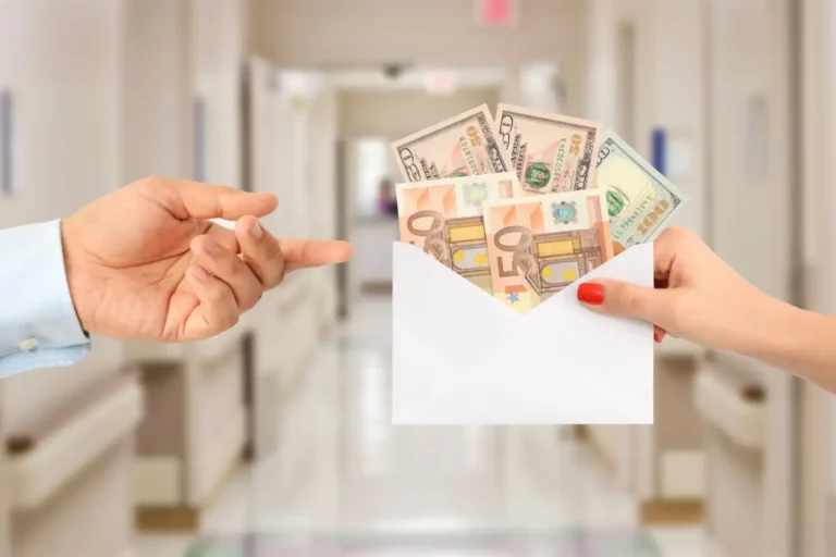 Zwei Hände in einem Krankenhausflur – eine hält einen Umschlag mit Euro- und US-Dollar-Scheinen, die andere zeigt darauf.