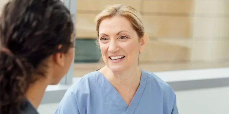Pflegekraft in Dienstkleidung führt freundliches Gespräch mit zugewandter Person.