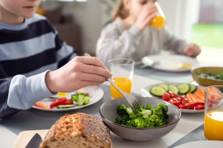Kinder essen gesundes Frühstück mit Gemüse, Brot und Orangensaft.