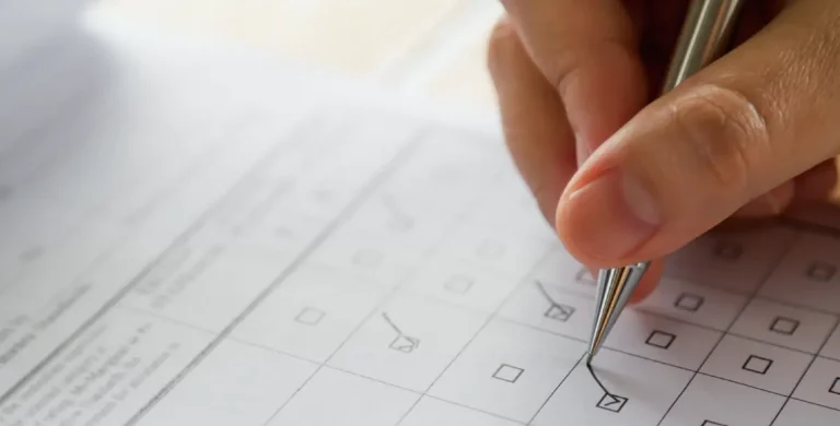 Hand mit Kugelschreiber kreuzt Kästchen auf einem Formular an.