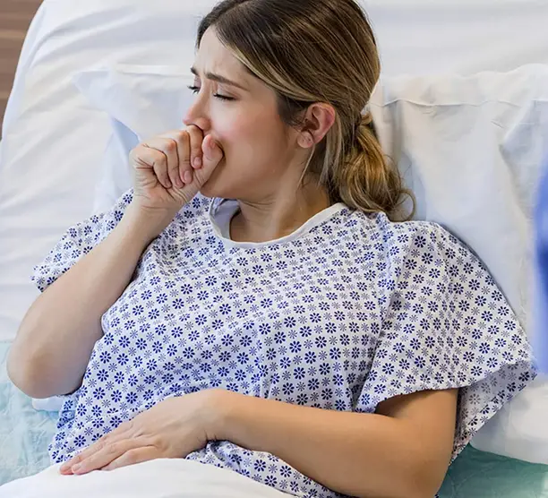 Person im Krankenhausbett hält sich hustend die Hand vor den Mund.