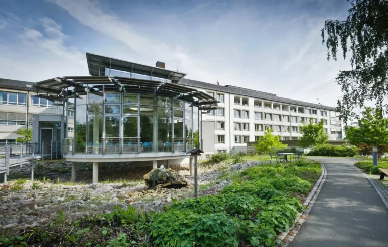 Modernes Pflege- oder Rehazentrum mit verglastem Pavillon und Gartenanlage.
