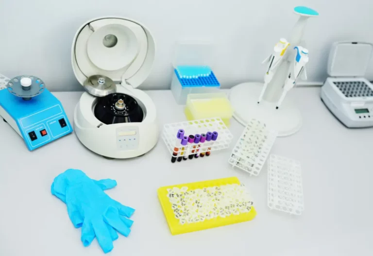 Labortisch mit Zentrifuge, Blutproben, Reagenzgläsern, Pipetten und blauen Einmalhandschuhen.