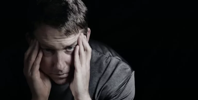 Mann wirkt gestresst oder emotional belastet, sitzt im Halbdunkel.