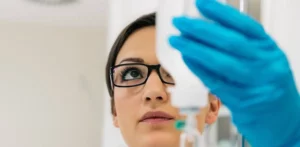 Pflegekraft mit Brille und blauen Handschuhen überprüft Infusionsflasche.