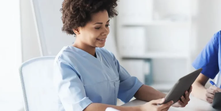 Pflegekraft in heller Dienstkleidung arbeitet mit einem Tablet.