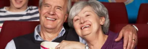 Älteres Paar lächelt und genießt gemeinsam Popcorn im Kino: Silberfilm - eine Initiative für die Integration von Menschen mit Demenz