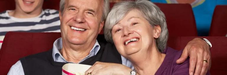 Älteres Paar lächelt und genießt gemeinsam Popcorn im Kino: Silberfilm - eine Initiative für die Integration von Menschen mit Demenz