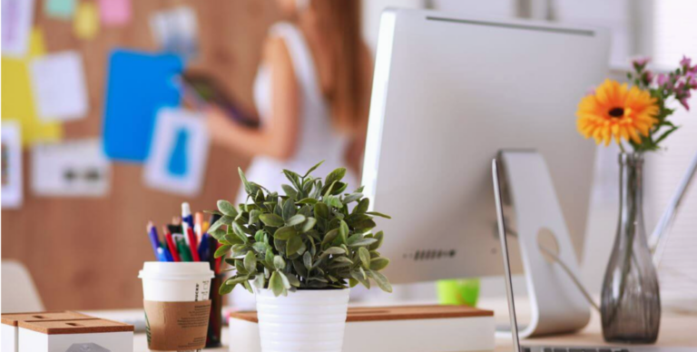 Ein stilvoller Schreibtisch mit einem Computer, einer Kaffeetasse und blühenden Blumen, perfekt für produktive Stunden.