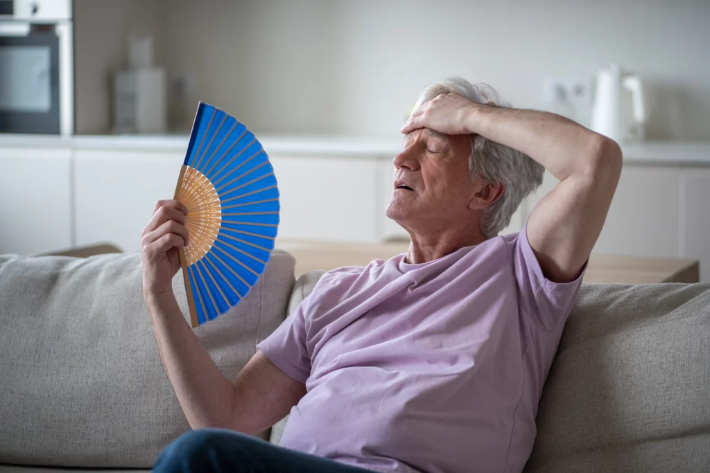 ein älterer Mann sitzt auf dem Sofa und wedelt mit einem Fächer vor sich her