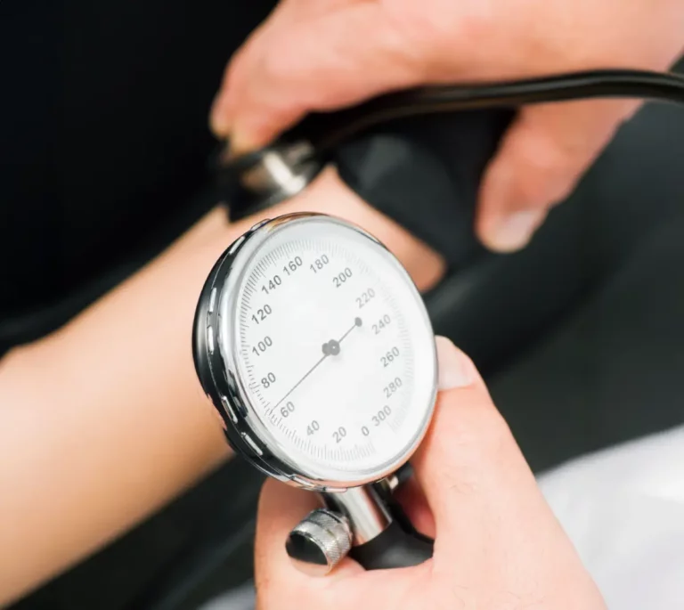 Person misst Blutdruck mit Manschette und analogem Messgerät am Oberarm.