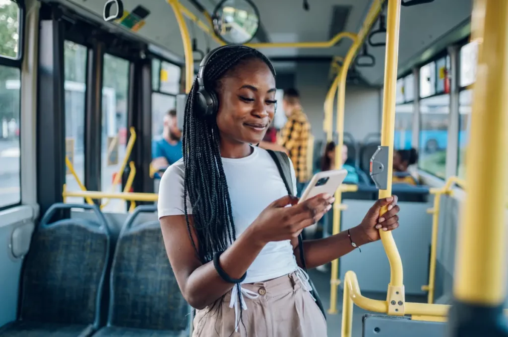 Frau mit Kopfhörern uns Handy in der Hand steht im Bus.