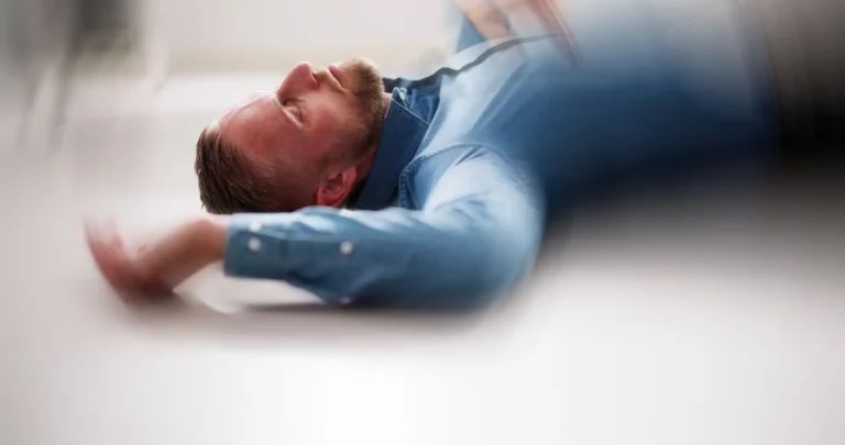 Person liegt am Boden in Innenraum, Augen geschlossen, Oberkörper sichtbar, Bild verschwommen