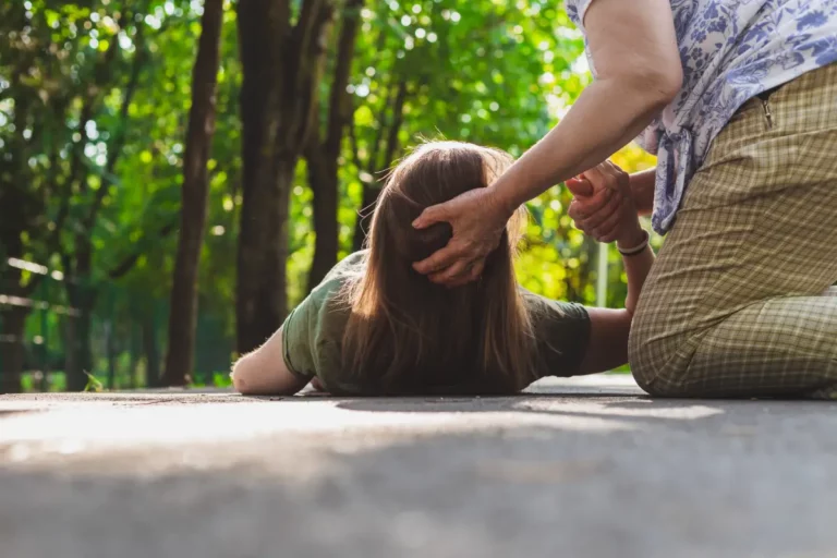 Person liegt auf dem Rücken auf einem Weg im Park, zweite Person kniet daneben.
