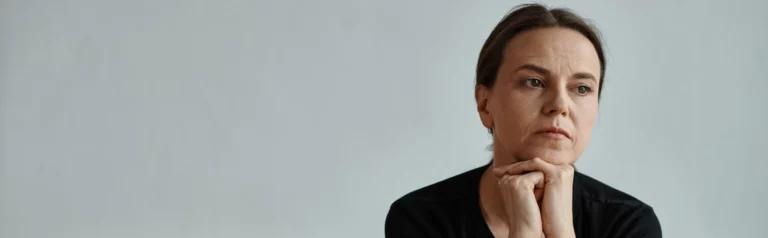 Person stützt das Kinn auf die Hände und blickt zur Seite.