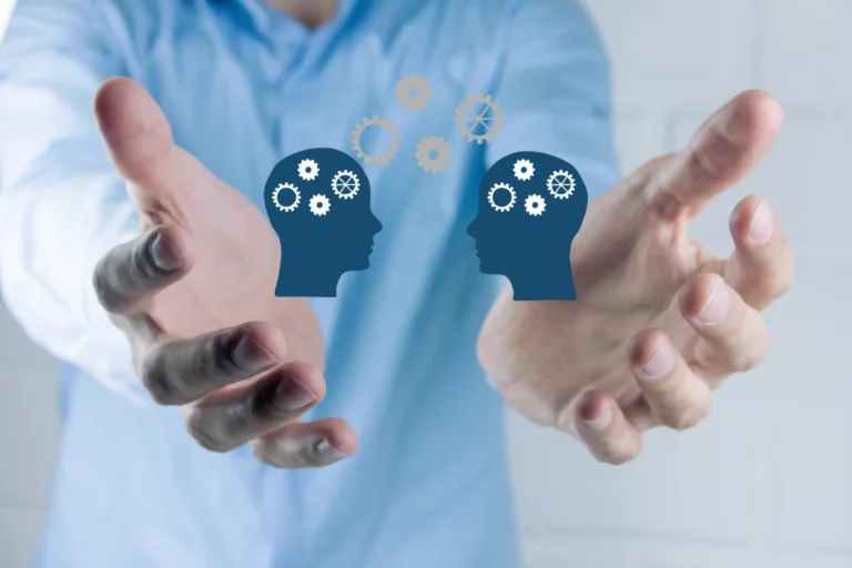 Person streckt Hände nach vorn; zwischen ihnen zwei Kopf-Symbole mit Zahnrädern und weiteren Zahnrädern darüber.