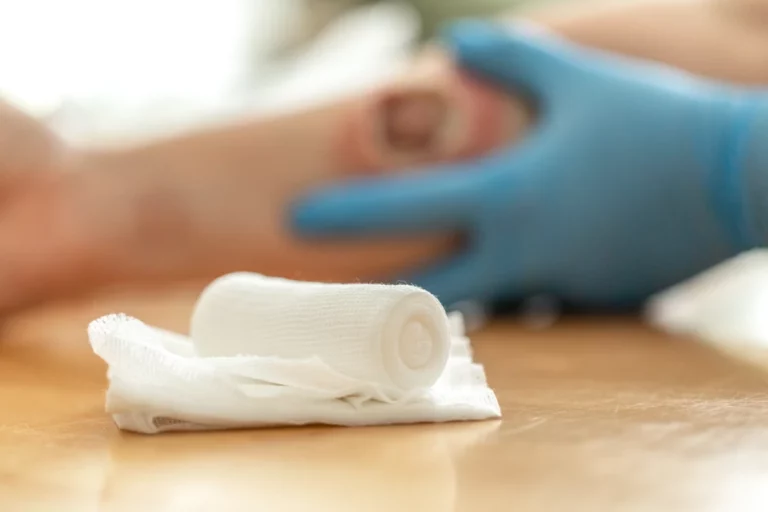 Nahaufnahme von Verbandmaterial, im Hintergrund Wundbehandlung am Unterarm.