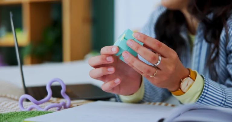 Person nutzt ein sensorisches Fidget-Spielzeug am Arbeitsplatz neben Laptop und Unterlagen.