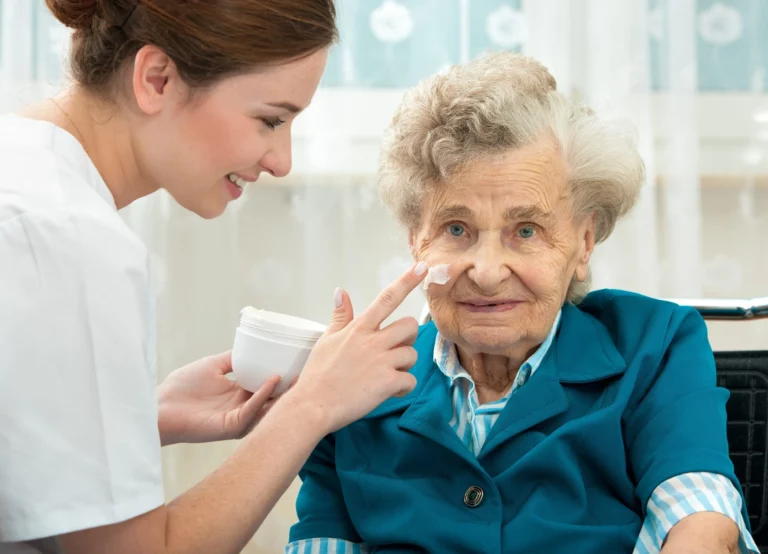 Auf diesem Bild sehen Sie einen Ausschnitt aus dem E-Learning-Kurs zum Thema Hygiene in der ambulanten Pflege. Auf dem Bild ist eine ältere Frau zu sehen, der von einer Pflegerin das Gesicht eingecremt wird.