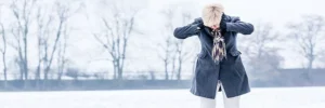Ältere Frau steht frierend im Schnee – Unterkühlung im Alter