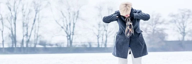 Ältere Frau steht frierend im Schnee – Unterkühlung im Alter