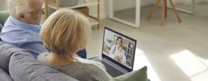 Senioren Paar sitzen auf der Couch und habe eine Online-Sprechstunde über den Laptop mit der Ärztin